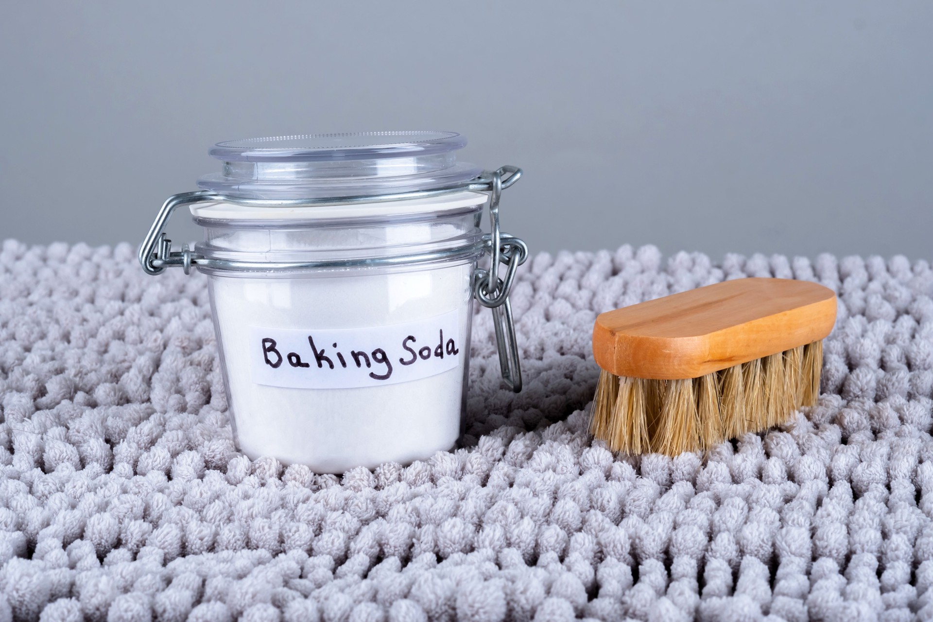 Baking soda and wooden cleaning brush on a gray carpet at home.